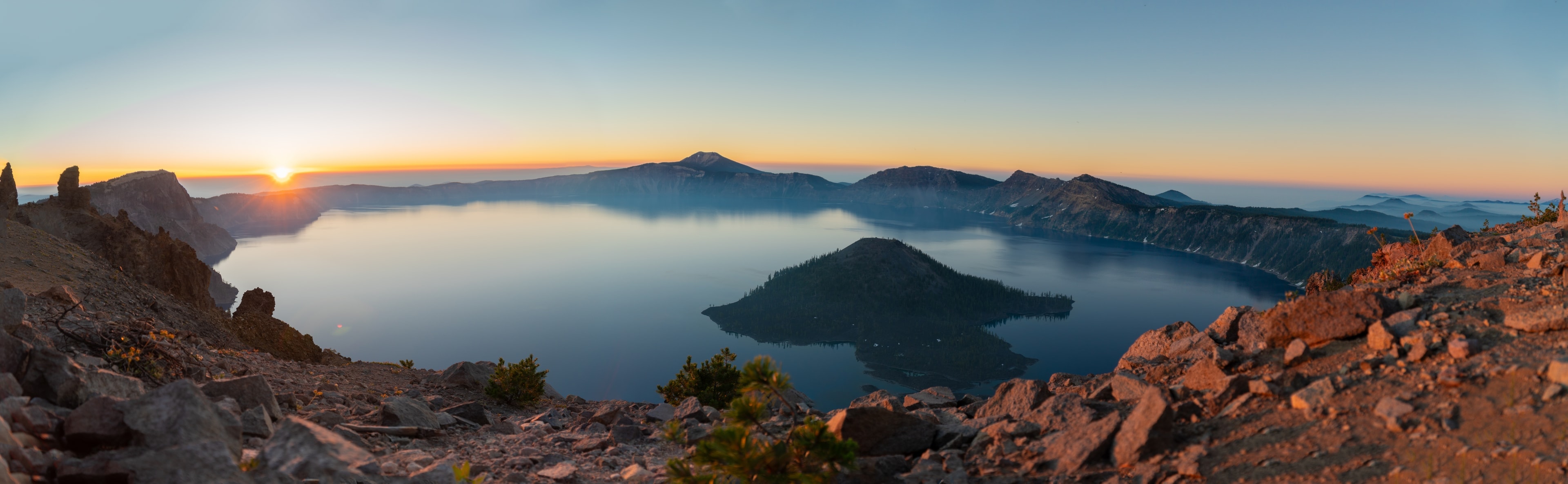 The sun rising over the rim of Crater Lake in July, Wizard Island dark in the still water
