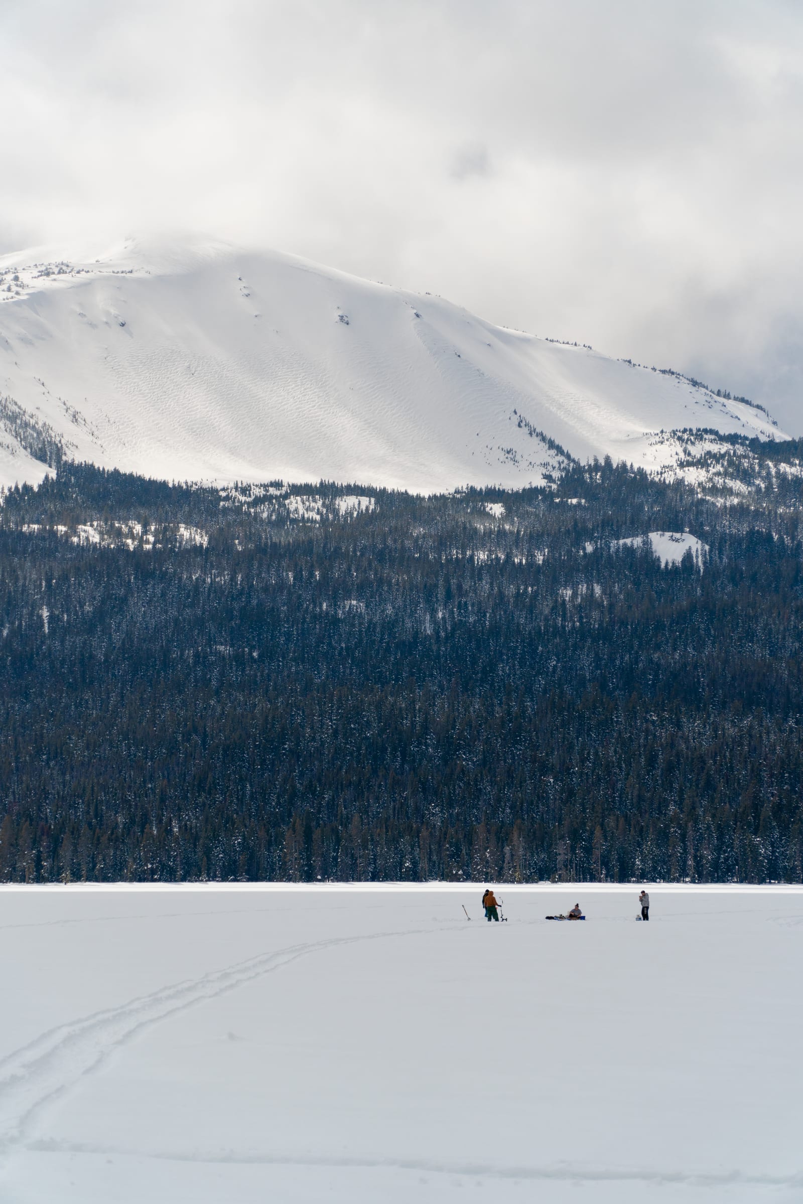 A few people ice fishing far out on frozen Diamond Lake in March, snowy Mount Bailey above the forest