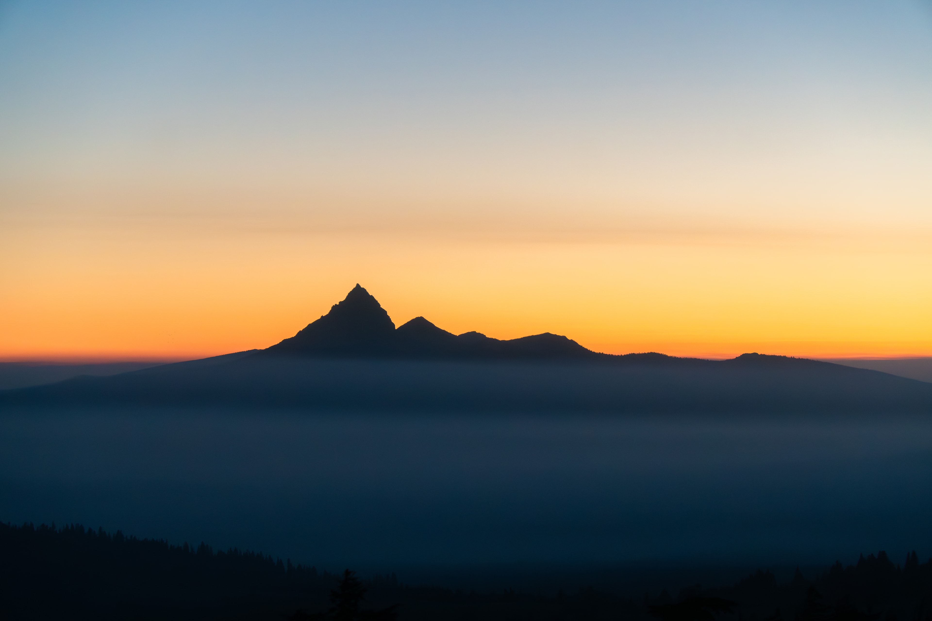 The dark peak of Mount Thielsen against an orange July sunrise, seen from the rim of Crater Lake