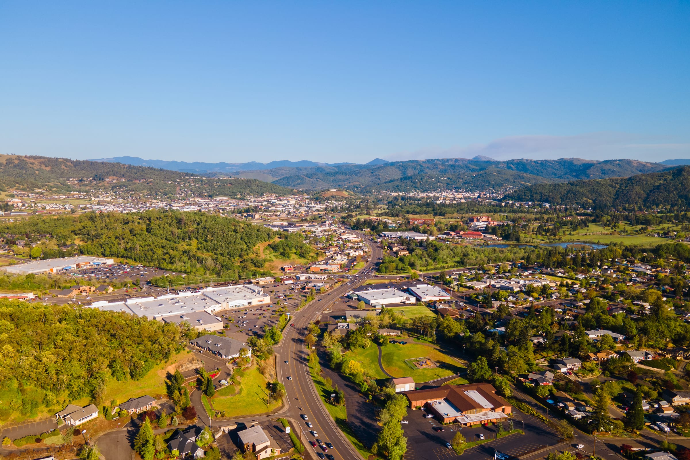 Roseburg from the air in April, streets and green trees spread across the valley under wooded hills