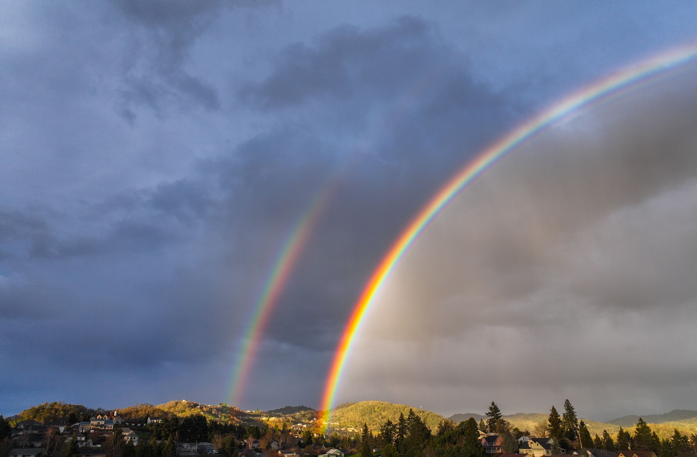 A double rainbow arching over the houses and hills of Roseburg under a grey February sky