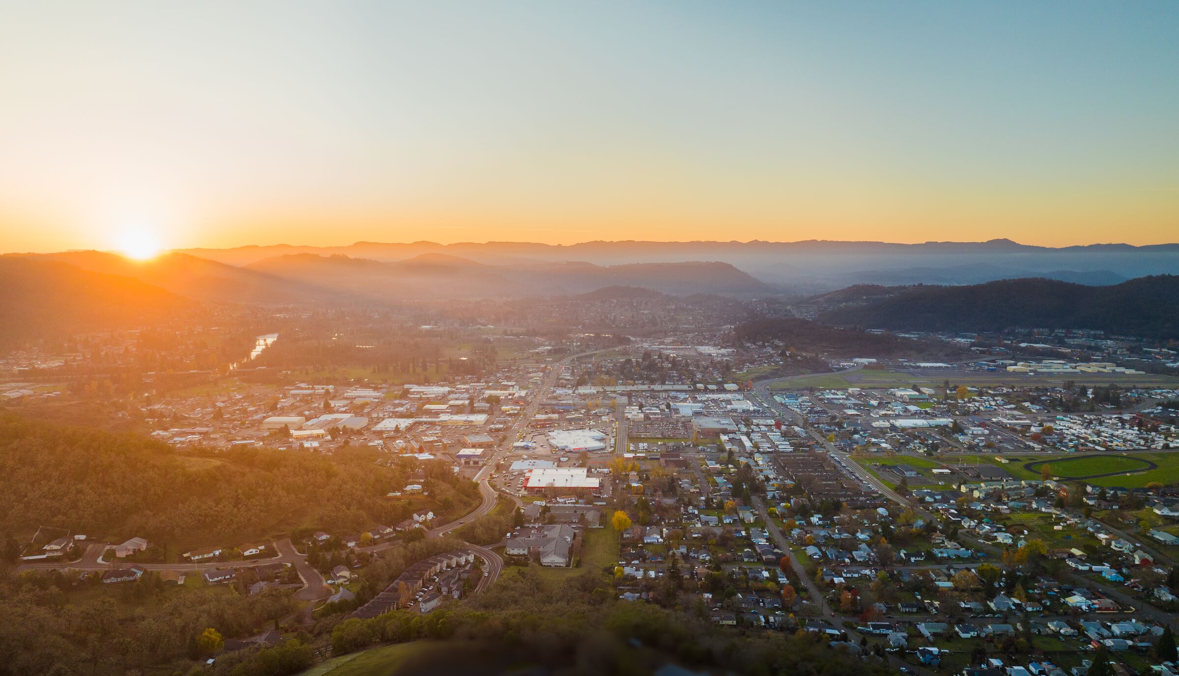 The November sun setting behind the hills at Roseburg, the whole town spread across the valley in golden light, seen from the air