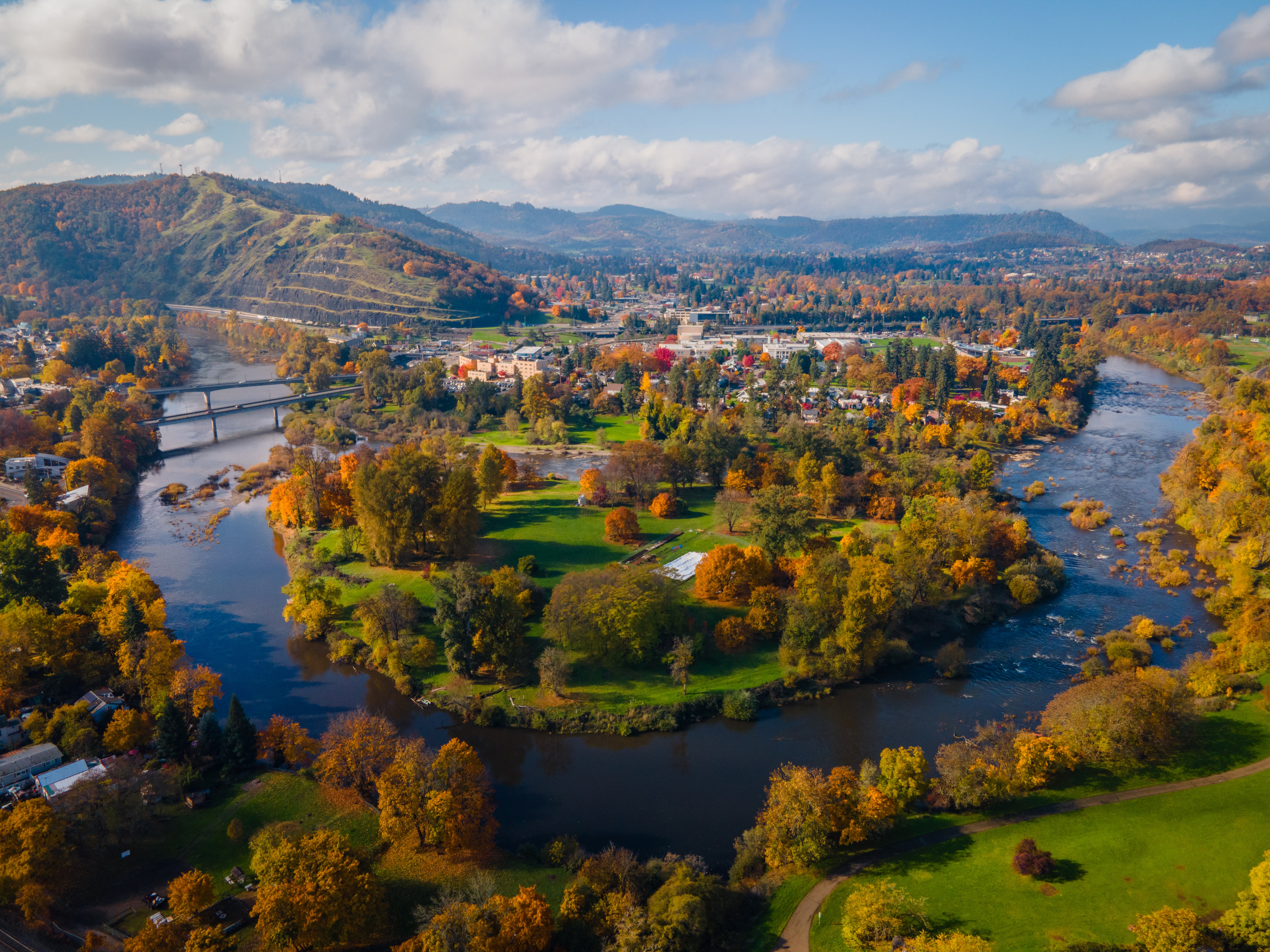 The South Umpqua River bending around green lawns and yellow autumn trees in Roseburg, seen from the air in November, hills beyond