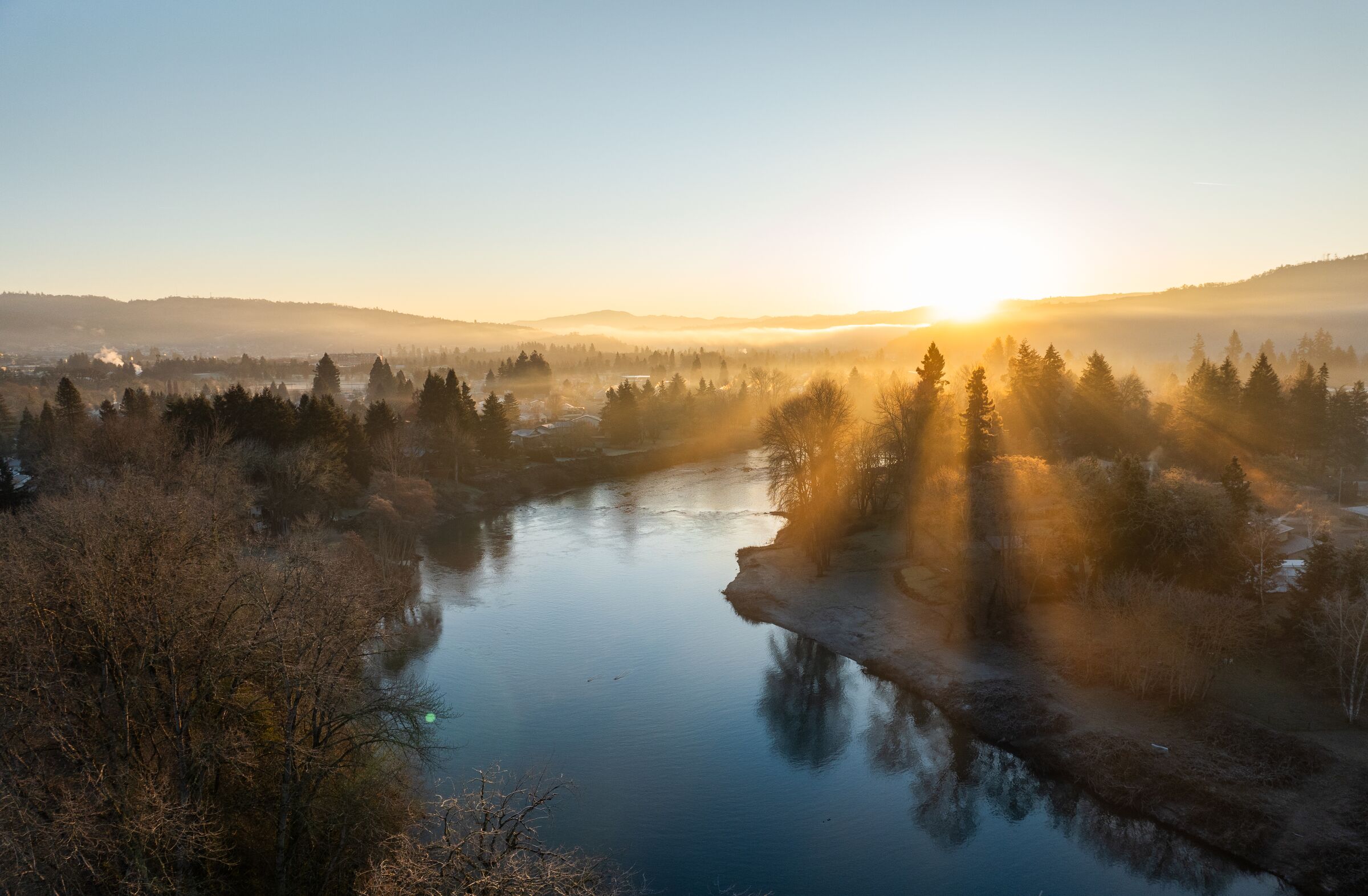 The January sun rising through fog over the South Umpqua River at Roseburg, bare trees along the banks