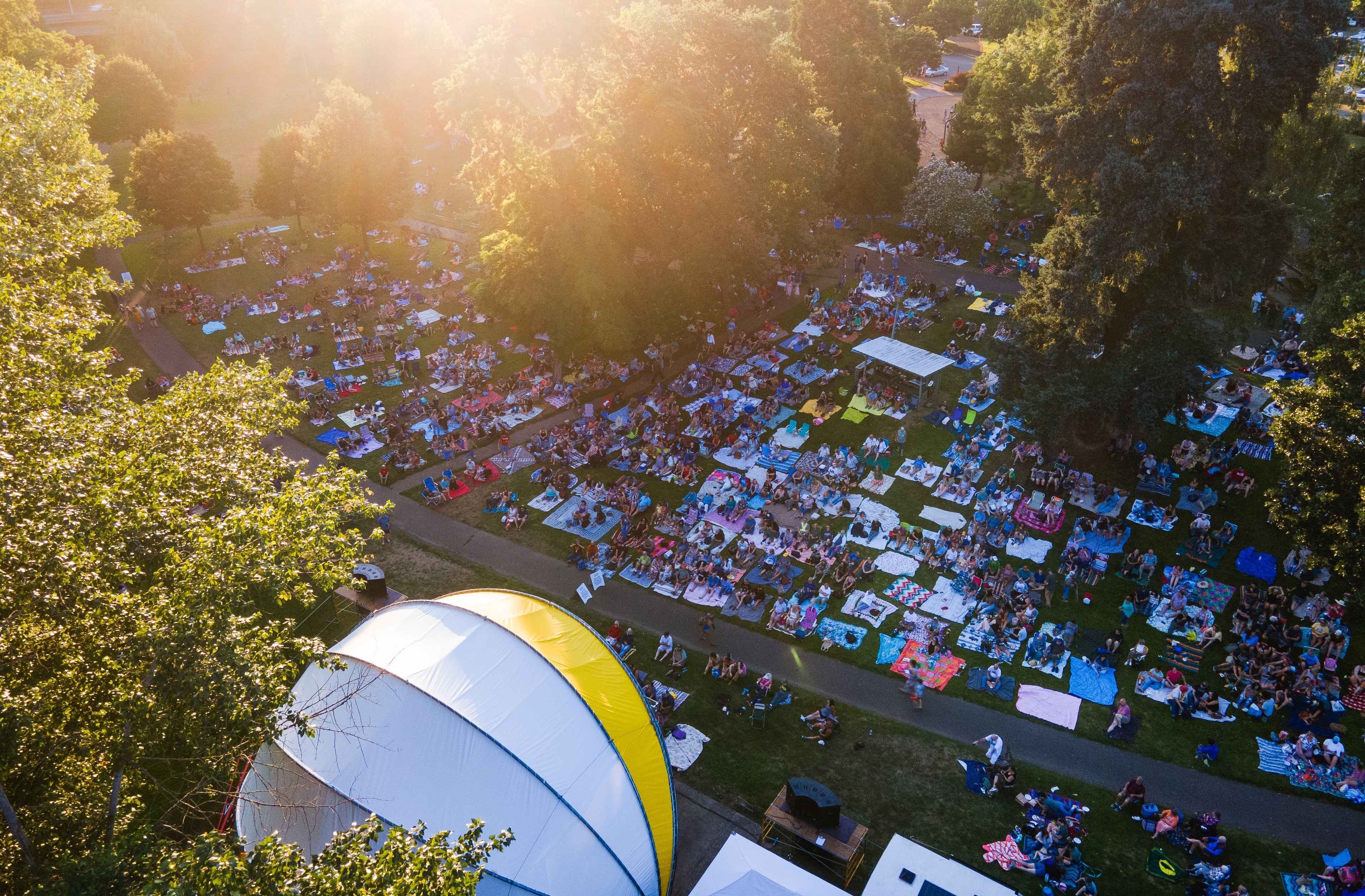 A crowd on blankets on the lawn at Stewart Park for a summer concert, the band shell at the front, seen from the air