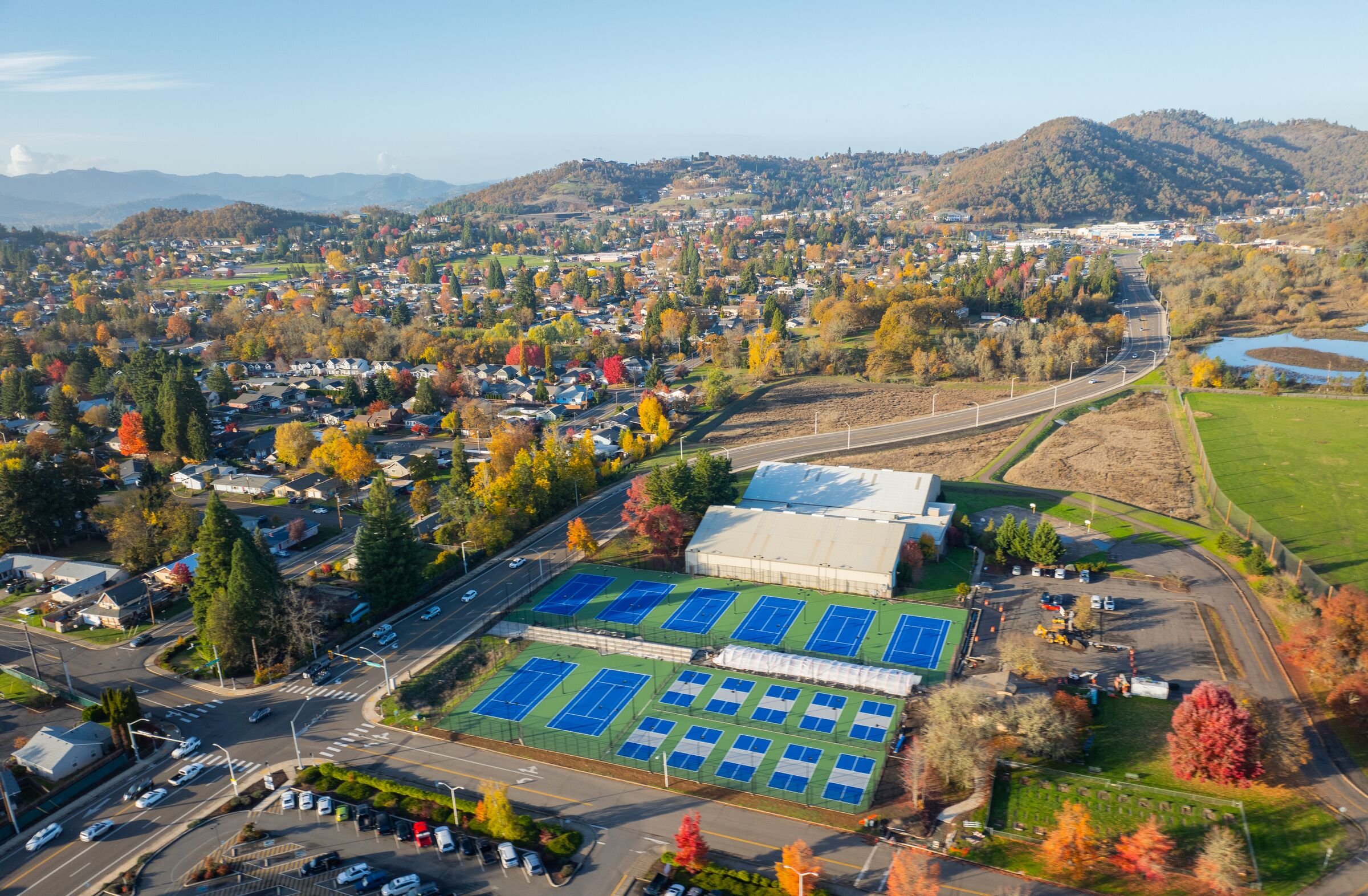 Blue courts at Stewart Park from the air in November, autumn trees and the town beyond