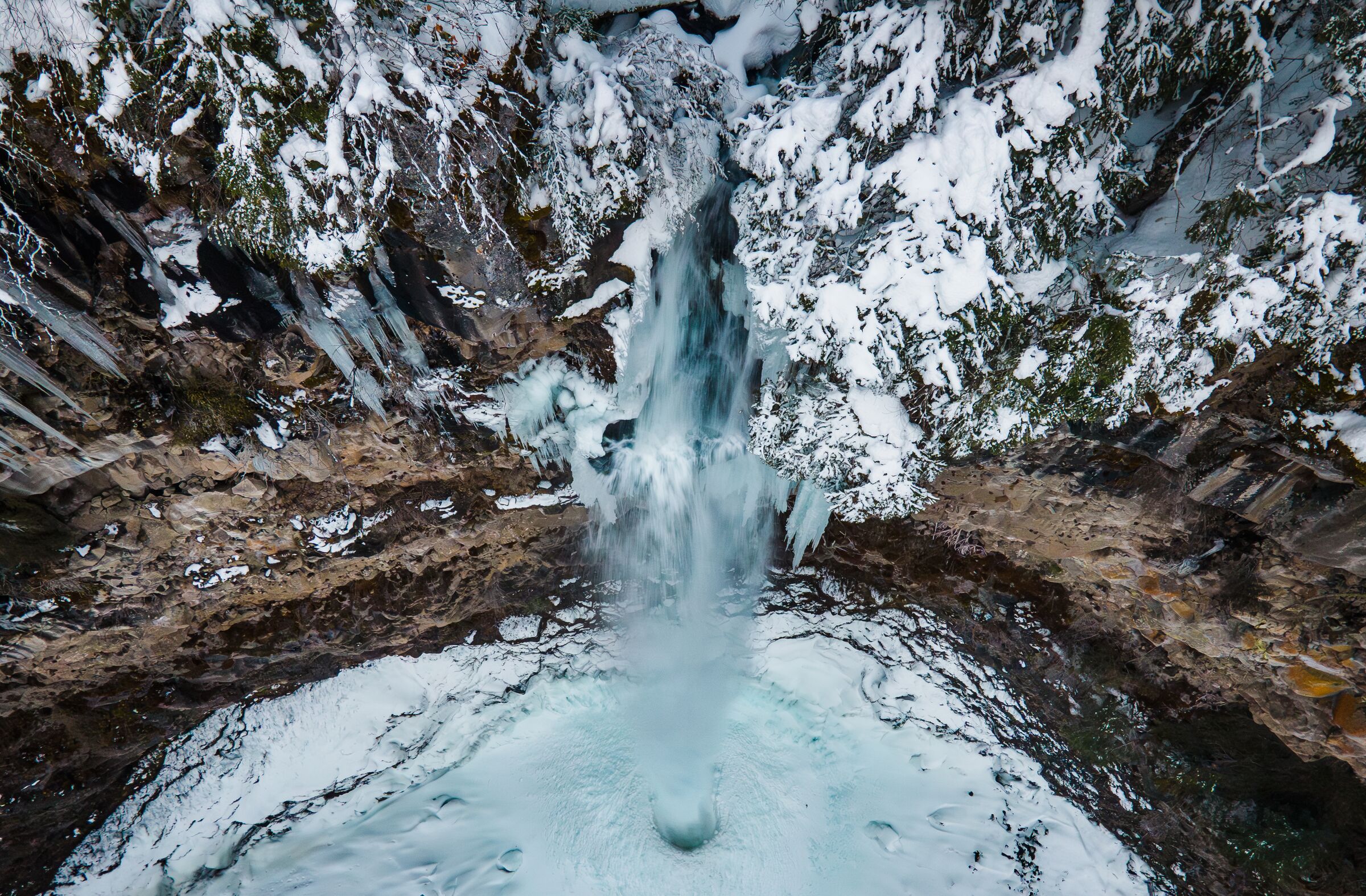 Watson Falls in March from above, its pool frozen white and the cliff edges under snow